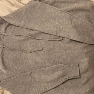 Grå hoodie - Säljer en klassisk grå merino ull hoodie med justerbar dragsko i huvan. Perfekt för en avslappnad stil och passar till det mesta. Mjukt material och ribbade muddar vid ärmslut och nederkant. Den är helt oanvänd eftersom jag köpte den i fel storlek.