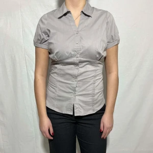 Grå kortärmad blus - Snygg grå blus med korta ärmar och knappar framtill. Perfekt för en stilren look.