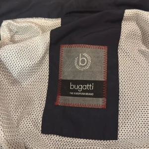 Svart jacka från Bugatti - Snygg svart jacka från Bugatti med dragkedja och hög krage. Jackan har en stilren design med en bröstficka och två sidofickor. Perfekt för en stilren look.