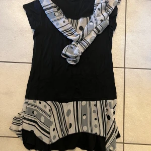 Svart och grå topp  med mönster - Trendig kortklänning i svart med grått mönster av prickar och ränder. Klänningen har en unik design med asymmetriska detaljer och en matchande sjal. Perfekt för en stilfull look.