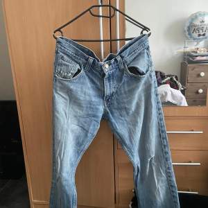 Säljer ett par klassiska blå jeans från Lee. De har en snygg, sliten look med några små slitningar som ger dem en cool vintage-känsla. Perfekta för en avslappnad stil. De har en knappgylf och är i ett bekvämt material.