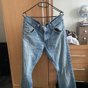 Blå jeans från Lee - Säljer ett par klassiska blå jeans från Lee. De har en snygg, sliten look med några små slitningar som ger dem en cool vintage-känsla. Perfekta för en avslappnad stil. De har en knappgylf och är i ett bekvämt material.
