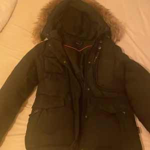 Hollies jacka  - En väldigt fin och modern jacka som inte gått ur stil än med äkta pälskrage vid luvan. Använd ett fåtal gånger och är precis som ny, stl 40 men passar en som har stl S i vanliga fall. Pris går att diskuteras!