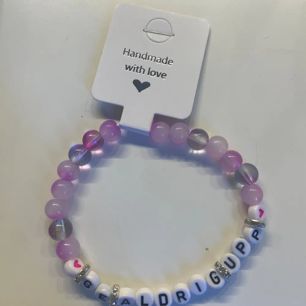 Ett supergulligt handgjort armband med kärlek! Det har pärlor i olika nyanser av lila och rosa, och bokstavspärlor som bildar texten 'GE ALDRIG UPP'. Perfekt som en peppande accessoar eller present till någon speciell. 💜. Accessoarer.