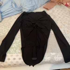 Svart långärmad topp med knyt - Säljer en elegant svart långärmad topp med en snygg knytdetalj framtill. Perfekt för både vardag och festliga tillfällen. Toppen har en tight passform och är gjord i ett mjukt och bekvämt material.