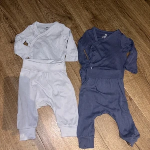 Tvådelade babyset i vitt och blått - Säljer två söta och bekväma babyset från H&M. Ett set är i ljus blå och det andra i blått, båda med långärmad överdel och matchande byxor. Perfekta för mysiga dagar hemma. Materialet är mjukt och skönt för bebisens hud.