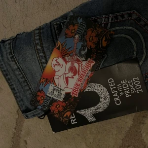 Blåa jeans från True Religion - Snygga blå jeans från True Religion med slitna detaljer och kontrastsömmar. De har en klassisk femficksdesign och en knappgylf. Perfekta för en avslappnad stil.