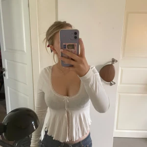 Vit långärmad topp från Gina Tricot - Säljer en söt vit långärmad topp från Gina Tricot. Toppen har spetsdetaljer runt halsen och en liten rosett framtill, en ”slits” vid magen 