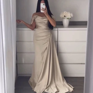 Champagnefärgad långklänning - Elegant champagnefärgad långklänning i satin med offshoulder-design. Köpte för 2000kr säljer för 1100kr. Använd en gång. XS/S