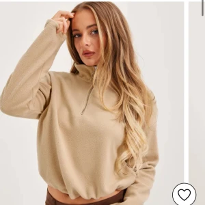 Beige fleece tröja med dragkedja - Säljer en mysig beige fleece tröja med halv dragkedja och hög krage. Perfekt för kyliga dagar. Tröjan har en avslappnad passform och långa ärmar. Skriv för bild på den klänning jag säljer. 