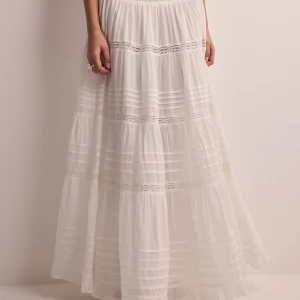 Vit långkjol från Neo Noir - Säljer en vacker vit långkjol från Neo Noir i 100% hållbar bomull. Kjolen har fina spetsdetaljer och en luftig design som passar perfekt för varma dagar. Den är tillverkad i Indien och har en elastisk midja för extra komfort.