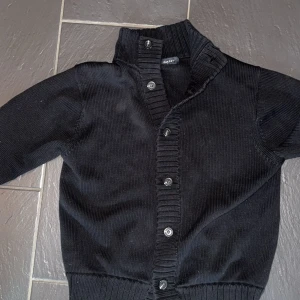  cardigan GANT - Säljer en stilren svart stickad kofta från GANT med knappar framtill. Perfekt för kyligare dagar🍾Skick 9,5 av 10 finns inget som visar på användning och jag har endast använt den 1-2 ggr 🥰