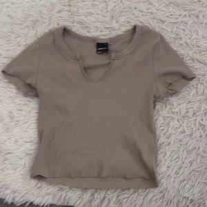 Beige ribbad topp från ginatricot - Säljer en beige ribbad topp från Bershka med korta ärmar och en v-ringad hals. Perfekt för en avslappnad stil. Toppen är i en neutral färg som passar till det mesta.