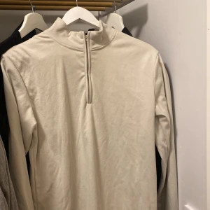 Beige långärmad tröja med dragkedja - Säljer en stilren beige långärmad tröja med dragkedja i halsen. Perfekt för kyligare dagar och enkel att matcha med olika outfits. Väldigt varm och skön.