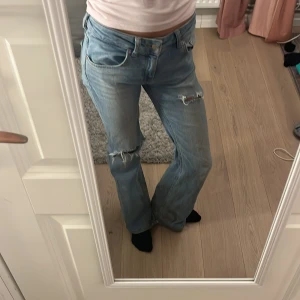 Blå jeans med slitningar - Snygga blå jeans med slitningar. De har en klassisk femficksdesign och en knappgylf. Perfekta för en avslappnad stil. De är lite slitna bak längst ner då jag har råkat trampa på de men de är jättefina annars. Jag säljer då de är lite stora för mig🥰