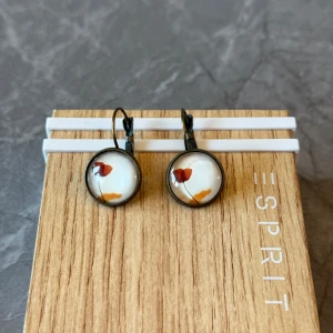 Örhängen i nyskick - Snygga örhängen med en rund design. De har en vit bakgrund med små färgdetaljer i rött och orange. Perfekta för att ge en subtil färgklick till din outfit.