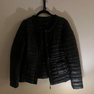 Svart quiltad jacka med pärldetaljer - Snygg svart quiltad jacka med pärldetaljer längs kragen och knäppningen. 
