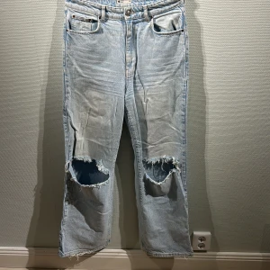Ljusa jeans med slitningar från Gina Tricot - Snygga ljusa jeans från Gina Tricot med slitningar på knäna för en trendig look. De har en klassisk femficksdesign och är tillverkade i denim. Perfekta för en avslappnad stil.