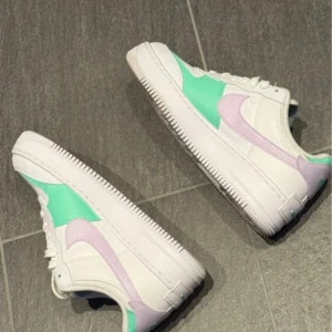 Nike Air Force i vitt och mintgrönt - Snygga Nike Air Force sneakers i vitt med mintgröna och ljuslila detaljer. Skorna har klassisk snörning och en bekväm sula. Perfekta för en stilren look med en färgglad twist.