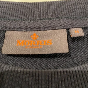 Mörkblå Morris tröja - Säljer en svart tröja från Morris med vit text och emblem på bröstet. Tröjan har långa ärmar och en rund halsringning. Perfekt för en stilren och avslappnad look.