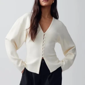 Vit kofta  - Säljer en stilren vit kofta med knappar framtill. Koftan har en v-ringad design och långa ärmar, perfekt för en elegant och avslappnad look.