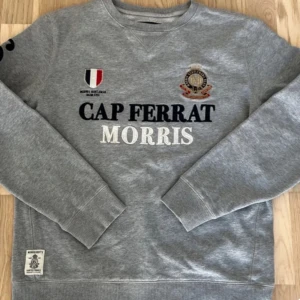 Grå sweatshirt från Morris - Säljer en unik stilren grå sweatshirt från Morris med broderad text 'Cap Ferrat' och 'Morris' på framsidan. Tröjan har långa ärmar. Pris kan diskuteras 
