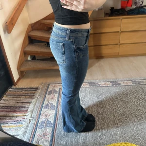 Blå bootcut jeans - Snygga blå bootcut jeans med låg midja. Klassisk design med fem fickor och dragkedja. Perfekta för en avslappnad stil. OBS! vid backfickan har det skapats ett hål men den har varit lagad. Efter ett tag så har ett till hål vid den andra fickan skapats men är inte lagad. Om man har en syra sjung så kan man sy ihop den. 🙂på byxan står det storlek 42 men det kan variera för jag är vanligtvis storlek 38. 