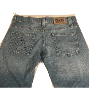 Blå jeans från D&G - Snygga blå jeans från D&G med dekorativa nitar och broderad logga på bakfickan. Jeansen har en klassisk femficksdesign och slitna detaljer för en trendig look. Perfekta för dig som vill ha en stilren men ändå unik stil. Tveka inte på att ställa frågor! Pris går att diskutera 