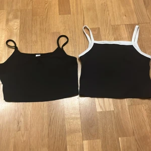Svarta linnen från H&M - Två svarta linnen från H&M. Ett med vita kanter och ett helt svart. Båda har smala axelband och är i en enkel design. Perfekta för en avslappnad stil.