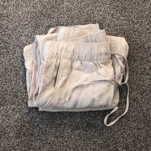 Beige linnebyxor från H&M - Säljer ett par bekväma beige linnebyxor från H&M. Byxorna har en elastisk midja med snörning för justerbar passform. De är i storleken S men är väldigt korta och väldigt luftiga, så jag hade nog sagt att de är i storlek XS. De är perfekta för en varm sommar dag eller en dag hemma.