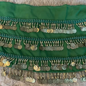 Grön danssjal med myntdetaljer - Säljer en grön danssjal dekorerad med silverfärgade mynt som ger ett härligt ljud när man rör sig. Perfekt för festliga tillfällen eller dansuppvisningar. Sjalen är i ett lätt och luftigt material som faller fint.