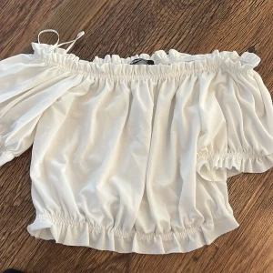 Vit offshoulder topp - Säljer en superfin vit offshoulder topp med elastiska kanter och volanger. Perfekt för sommardagar eller en festlig kväll. Materialet känns mjukt och luftigt, vilket gör den bekväm att bära. Passar bra till både jeans och kjol!