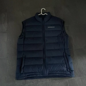 Mörkblå dunväst från Peak Performance - Säljer en snygg mörkblå dunväst från Peak Performance. Västen har en dragkedja framtill och är perfekt för kyliga dagar. Den är i mycket bra skick och passar bra till både höst och vår. Perfekt för lager-på-lager-stil!