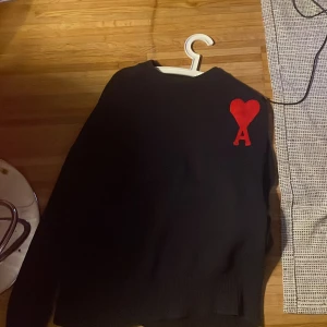 Svart tröja från Ami - Säljer en snygg svart tröja från Ami med ett rött hjärta och bokstaven A på bröstet. Tröjan är i mycket bra skick och har långa ärmar. Perfekt för höst och vinter! 🖤❤️