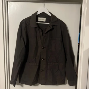 Mörkgrön overshirt från A Days March - Säljer en stilren mörkgrön jacka från A Days March storlek M. Den har en klassisk krage och knappar framtill. Perfekt för höst och vår, med en normal passform och långa ärmar. Jackan är i bra skick men däremot saknas en knapp och samt småfläckar som enkelt går bort i tvätten. Nypris 1500kr