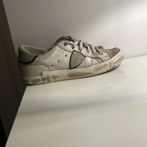 Vita sneakers med grå detaljer - Säljer ett par vita sneakers från Philippe Model i acceptabelt skick. Skorna har grå detaljer och snörning. De är lite slitna men fortfarande bekväma och perfekta för vardagsbruk. Sulorna är svarta och har bra grepp. Passar bra till både jeans och shorts!