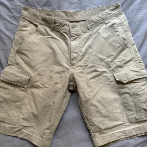 Vintage Peak Performance Beige Cargo Shorts - Beige vintage cargo shorts från Peak Performance, flitigt använda men väl omhändertagna. Naturlig slitage vid benöppning (se bild) Köpta i vintagebutik för ca 200kr, men säljer då de ej kommit till använding (L: 55cm, W: 46cm, Innersöm: 28cm, Benöppning: 30cm)