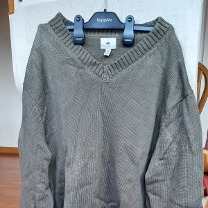 Olivgrön stickad tröja från H&M - Säljer en mysig olivgrön stickad tröja från H&M. Den har en v-ringad hals och långa ärmar, perfekt för kyliga dagar. Praktiskt sätt ny