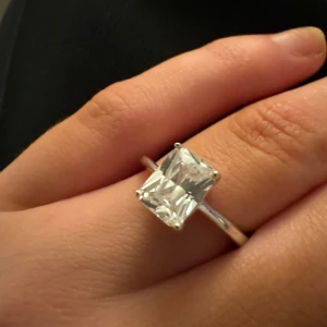 Elegant silverring med stor sten - Säljer en superfin silverring med en stor, rektangulär klar sten. Perfekt för att ge en touch av glamour till vilken outfit som helst. Ringen är i mycket bra skick och passar perfekt för speciella tillfällen eller vardagslyx.