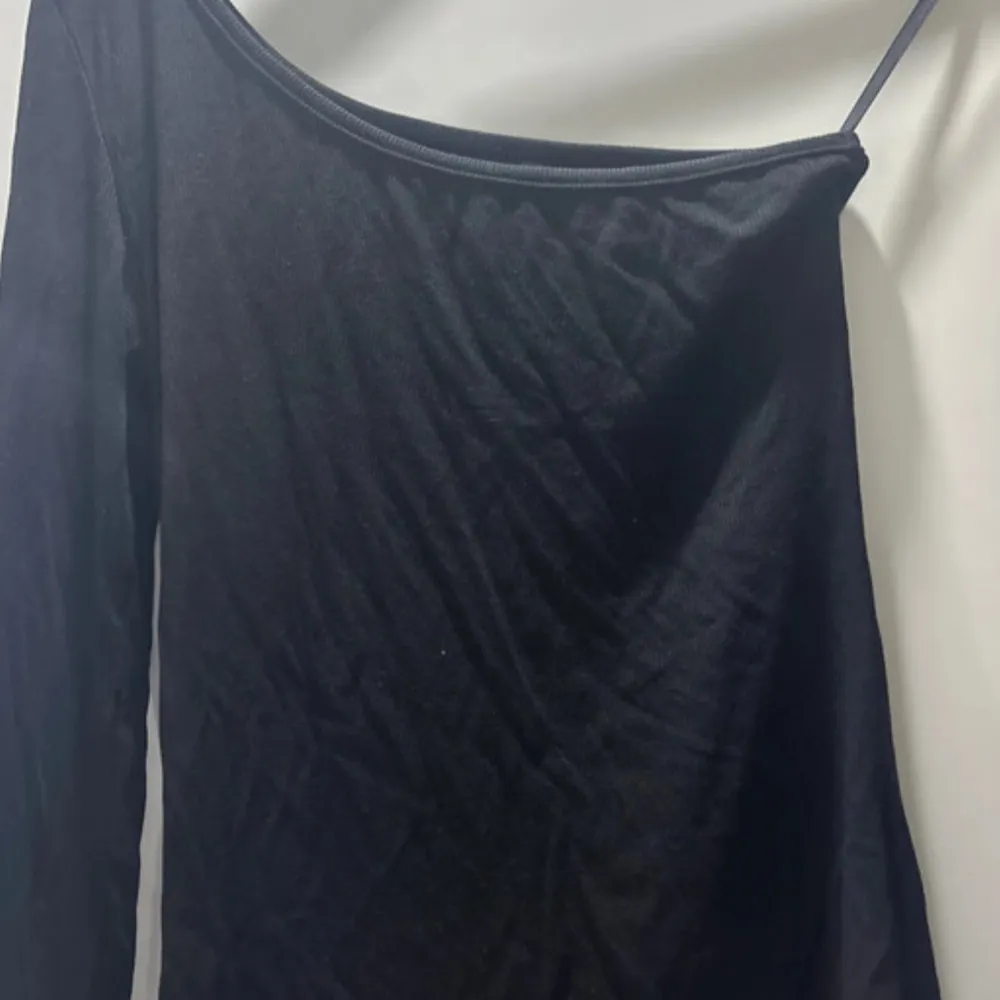 Snygg svart oneshoulder topp i ett mjukt och stretchigt material. Perfekt för en utekväll eller fest. Den har en tight passform som framhäver figuren och en stilren design som gör den lätt att matcha med accessoarer.. Blusar.