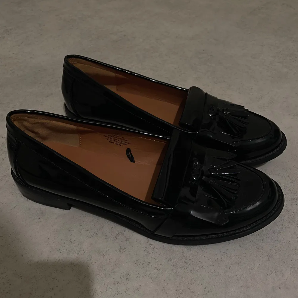 Snygga svarta loafers i skinn med dekorativa tofsar på ovansidan. Perfekta för både vardag och festliga tillfällen. De har en klassisk design med låg klack och en bekväm passform.. Skor.