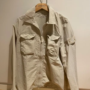 Beige Stone Island jacka - Säljer en snygg beige jacka från Stone Island. Den är i riktigt bra skick och storlek M. Perfekt för vår och höst! Kan inte garantera äkthet men koden går att skanna. Släng iväg ett prisförslag om priset inte passar.