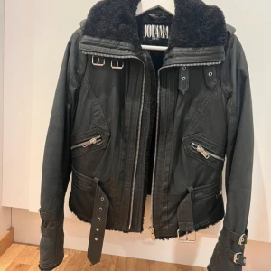 Svart jacka från Jofama by Kenza - Säljer en snygg svart jacka från Jofama by Kenza. Den har en cool bikerstil med dragkedjor och bältesdetaljer. Jackan är fodrad med mjuk pälsimitation för extra värme. Perfekt för höst och vinter! Storlek 40, men passar även 38. Otroligt sparsamt använd, inga defekter. 