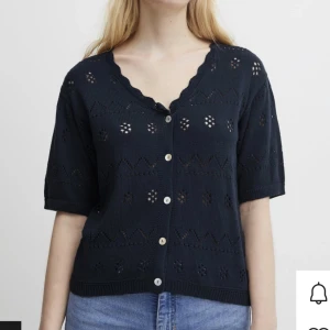 marinblå kofta med knappar - Säljer en marinblå kofta med kortärmad design och fina hålmönster. Den har en v-ringad hals och knappar framtill. Perfekt för vår och sommar, och kan enkelt matchas med jeans eller kjol. Koftan är i bra skick och redo för en ny ägare!