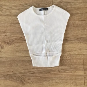 Vit ribbad topp - Säljer en superfin vit ribbad topp i storlek XXS. Perfekt för lager-på-lager eller som ett stilrent basplagg. Den är ärmlös och har en tight passform som framhäver figuren. Den har en slit vid magen som gör att magen syns. Toppen är i mycket bra skick och redo för nya äventyr!