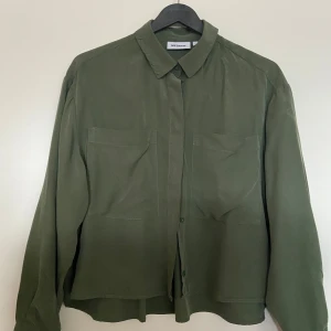 Olivgrön skjorta från Weekday - Säljer en stilren olivgrön skjorta från Weekday i storlek XS. Skjortan har långa ärmar och en klassisk krage. Den är tillverkad i ett mjukt material som känns skönt mot huden. En knapp saknas på ena ärmen men som ej behövs. Då det var en extra.