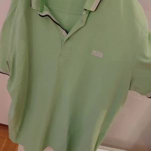 Grön pikétröja från Hugo Boss - Säljer en snygg grön pikétröja från Hugo Boss i regular fit. Perfekt för både vardag och lite finare tillfällen. Tröjan har en klassisk krage och korta ärmar. Den är i mycket bra skick och redo för en ny ägare. Passar perfekt till jeans eller chinos!