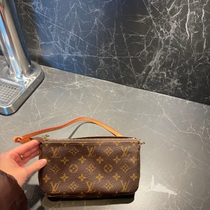 ÄKTA Louis Vuitton Pochette - Säljer min äkta Louis Vuitton Pochette, då den tyvärr inte kommer tills användning. Den är använd Max 5 ggr.  NY PRIS: 16.200kr. Kartong samt guldig kedja kommer med! (Fler bilder samt kvitto och äktehetsbevis kommer ikväll)  (kommer med låda)