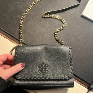 Tory Burch - Svart skinnväska med kedja - Snygg svart axelväska i skinn med en elegant kedja som axelrem. Väskan är i skinn och har dekorativa sömmar längs kanterna. Perfekt för både vardag och fest! 🖤
