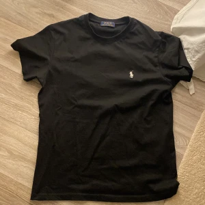 Svart t-shirt från Ralph Lauren - Säljer en klassisk svart t-shirt från Ralph Lauren i bomull. Den har en liten broderad logga på bröstet och är i mycket bra skick. Perfekt för både vardag och fest!
